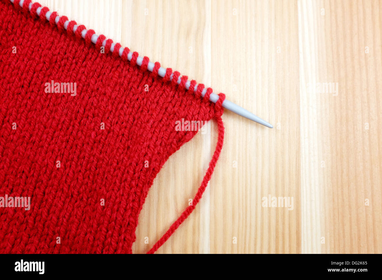 Stockinette stitch en lana roja sobre una aguja de tejer, sobre fondo de madera Foto de stock