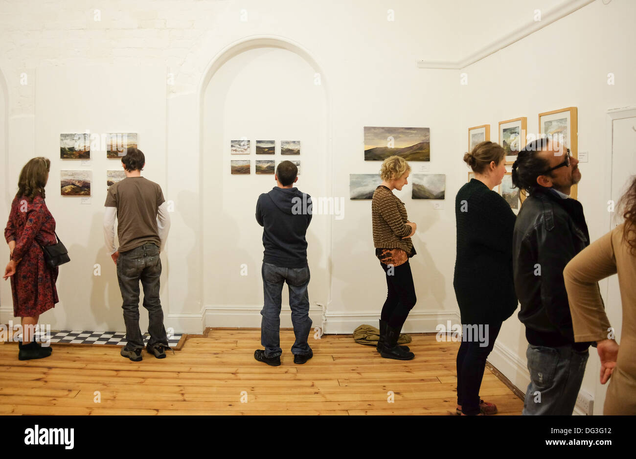 Un grupo de personas mirando las obras de arte en una exposición en una
