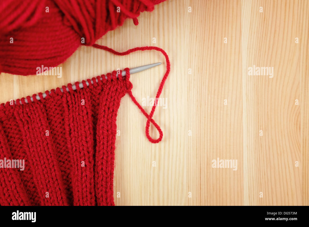 Rib rojo sobre el cosido con aguja de tejer una bola de lana, madera Foto de stock