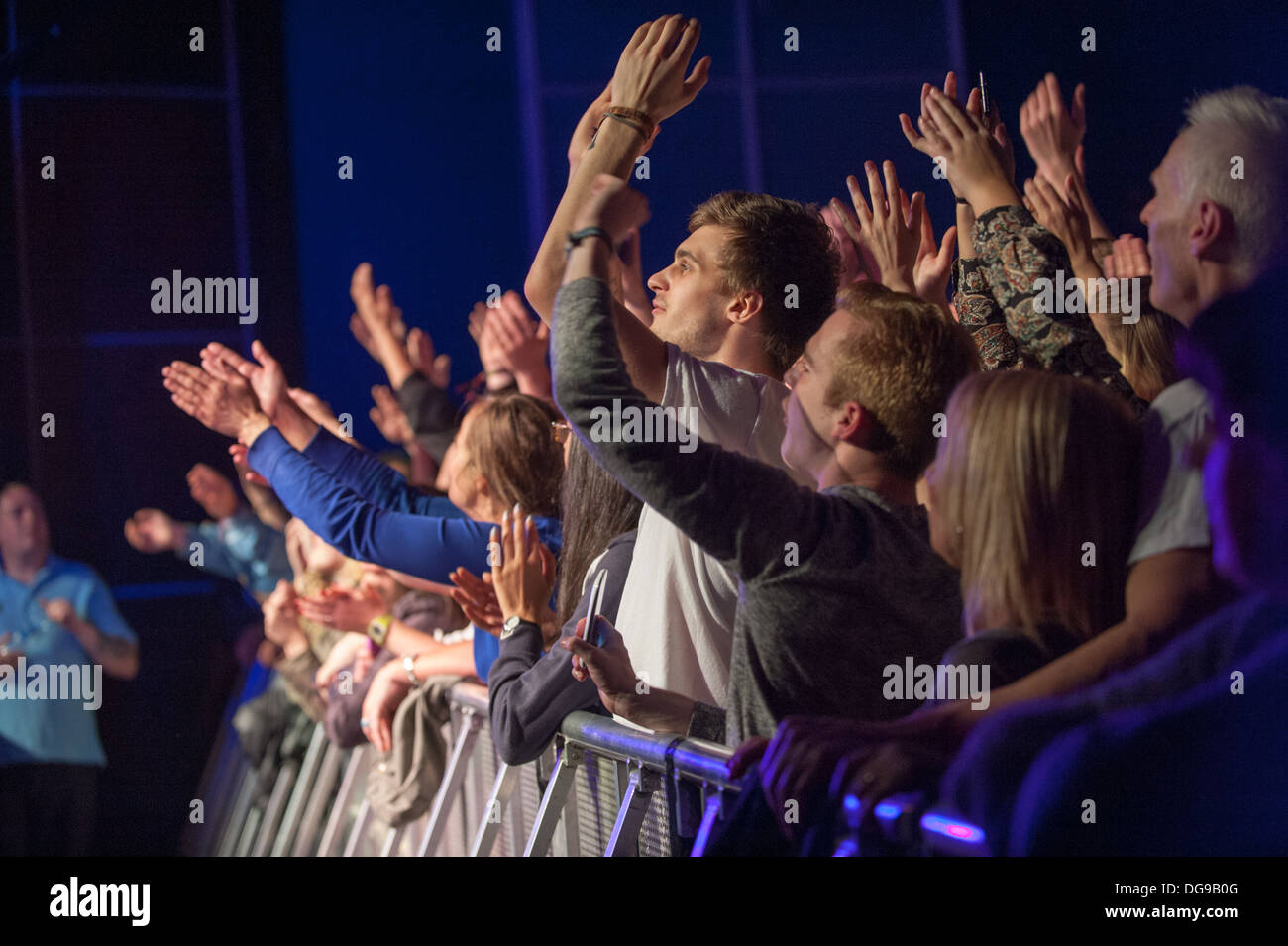 Jóvenes fans de la música en un concierto en vivo aplastado contra la barrera en el frente del escenario animando, aplaudiendo y gritando en una banda en el escenario Foto de stock