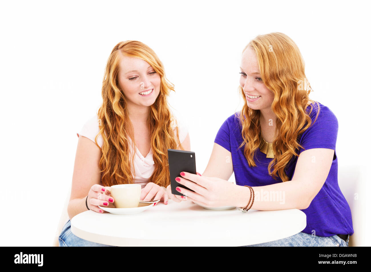 Dos sonriendo pelirroja mujer sentada en una mesa de café mirando un smartphone sobre fondo blanco. Foto de stock