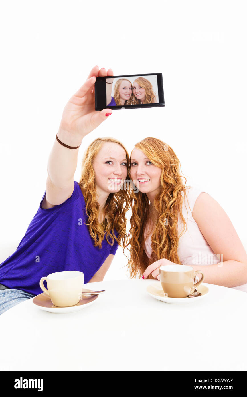 Feliz dos mujeres sentadas en una mesa de café haciendo fotos de sí mismos sobre fondo blanco. Foto de stock