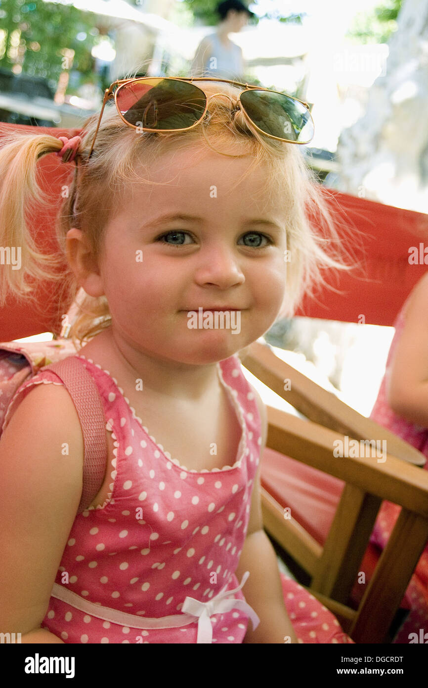 Niña de 3 años de edad sonriendo a la cámara, con gafas de sol sobre su cabeza en una cafetería al aire libre Fotografía stock - Alamy