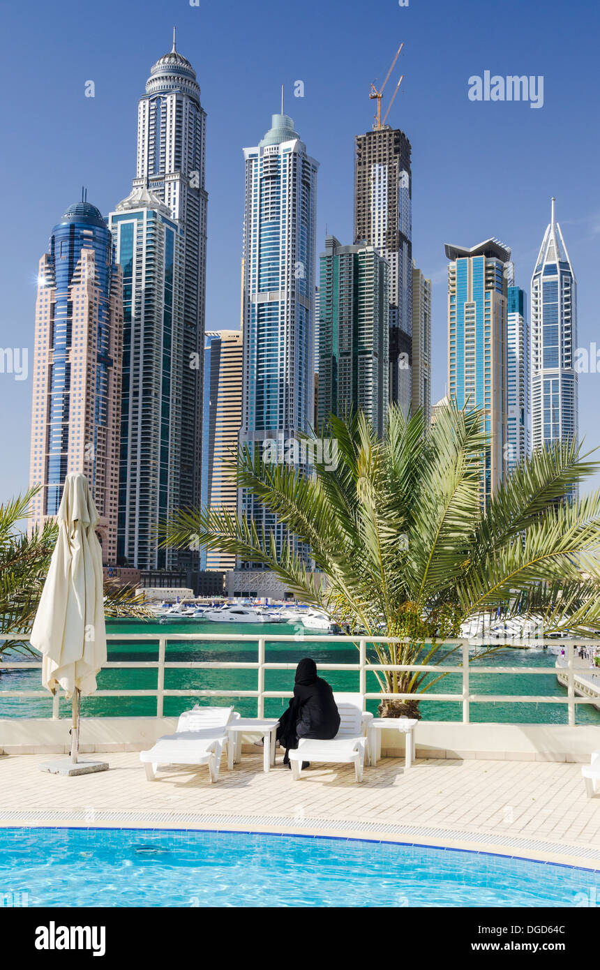 Una mujer vistiendo un chador mira sobre los rascacielos de Dubai Marina, desde la piscina del hotel, Dubai, Emiratos Árabes Unidos. Foto de stock