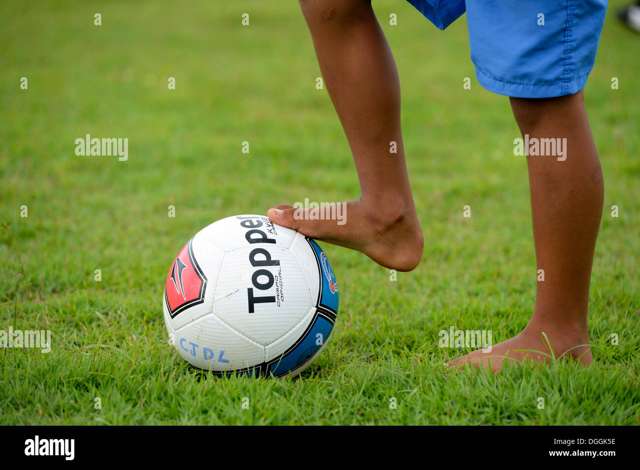 Muchacho descalzo, uno de los pies sobre una pelota de fútbol, proyecto social en una favela, Poxoréo, Mato Grosso, Brasil Foto de stock