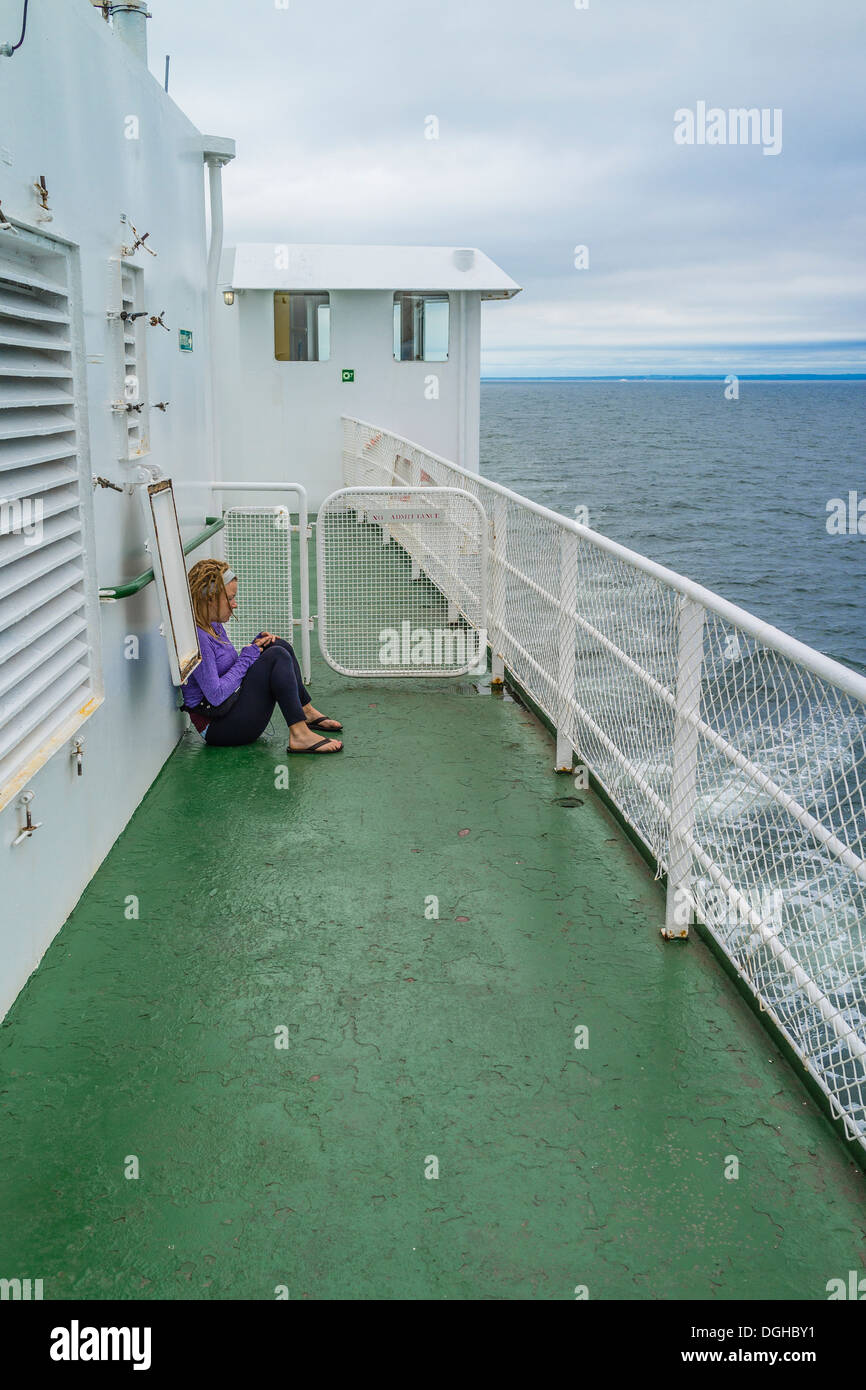 Mujer sentada sola, afuera en la cubierta de un ferry entre la Isla del Príncipe Eduardo y Nueva Escocia. Foto de stock