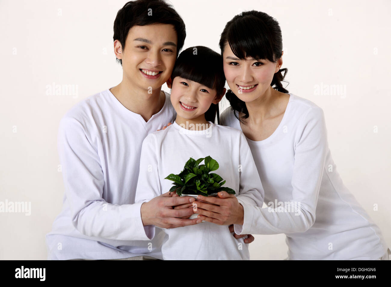 La familia de Asia oriental con un niño abrazando y sosteniendo la planta verde, sonriendo, mirando a la cámara Foto de stock