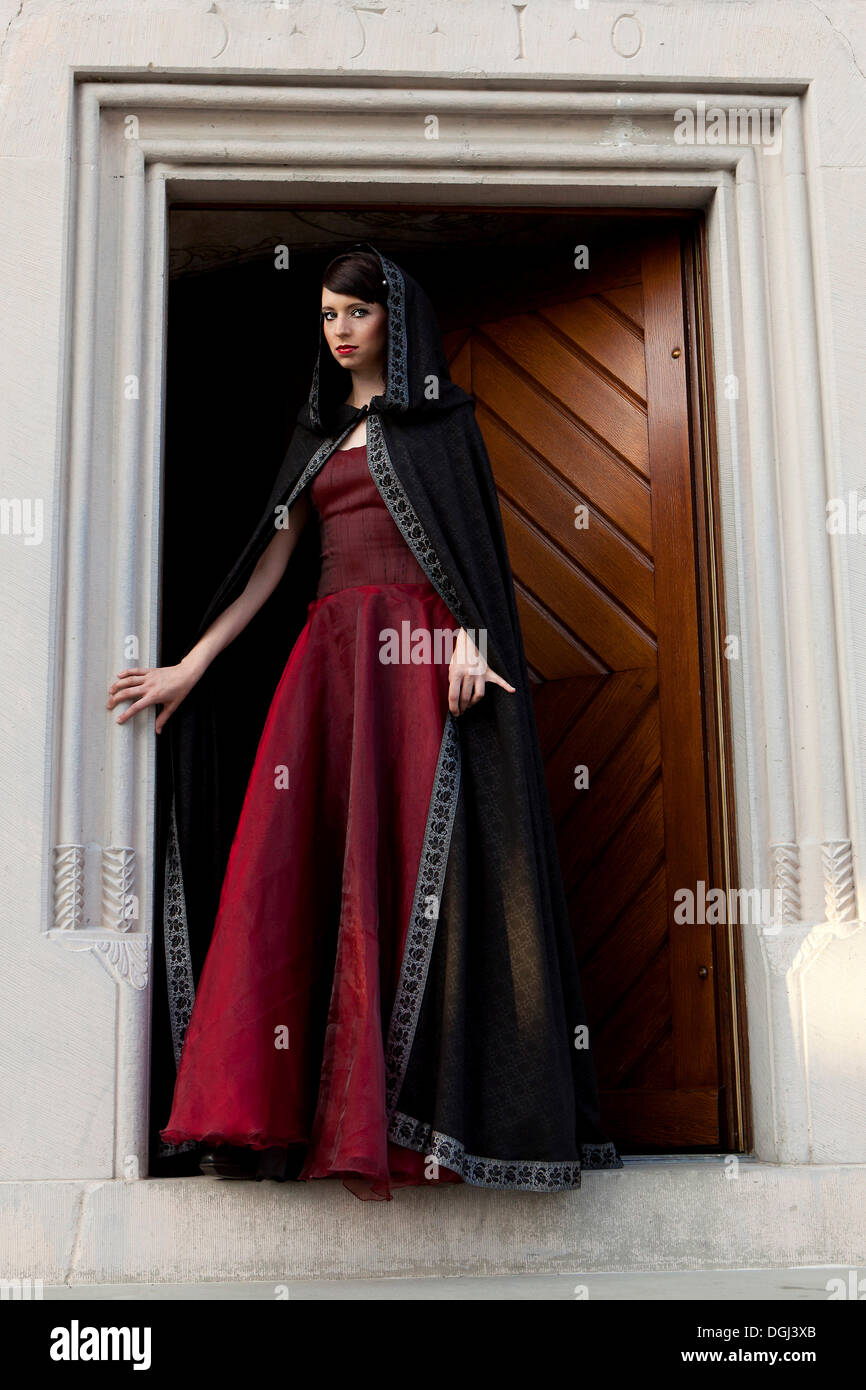 Mujer joven vistiendo un vestido rojo y una capa negra de pie en una puerta  Fotografía de stock - Alamy