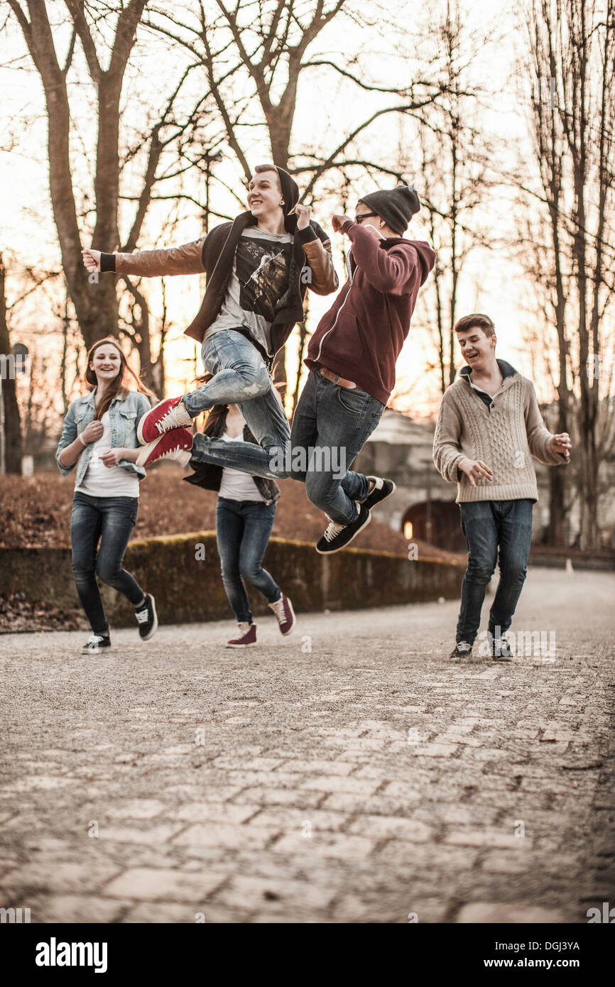 Cinco adolescentes jugando, saltando en estacionamiento Foto de stock