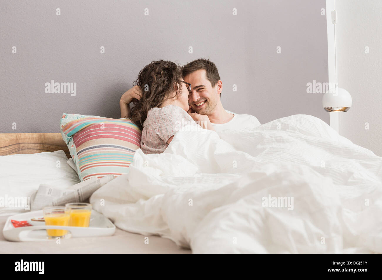 Adulto medio par acostado en la cama, desayuno en la bandeja Foto de stock