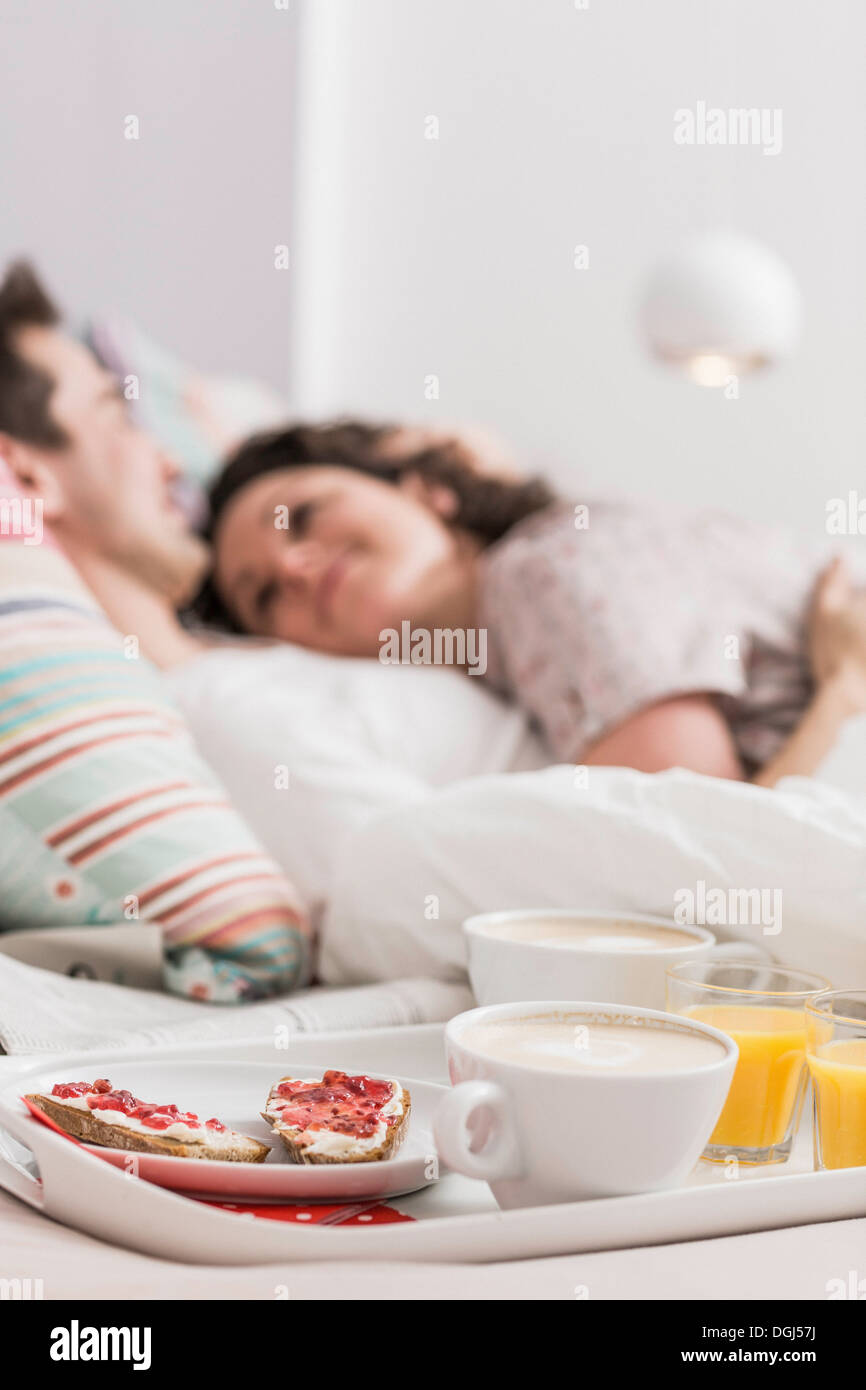 Adulto medio par acostado en la cama, desayuno en bandeja, abrazando Foto de stock