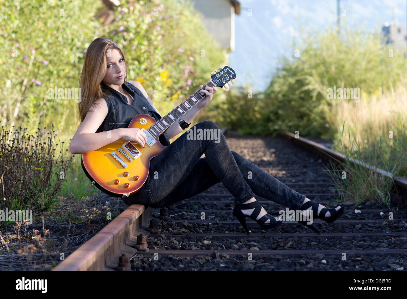 Mujer joven vistiendo pantalones vaqueros oscuros y tacones altos, sentado  con una guitarra eléctrica en una vía de ferrocarril Fotografía de stock -  Alamy