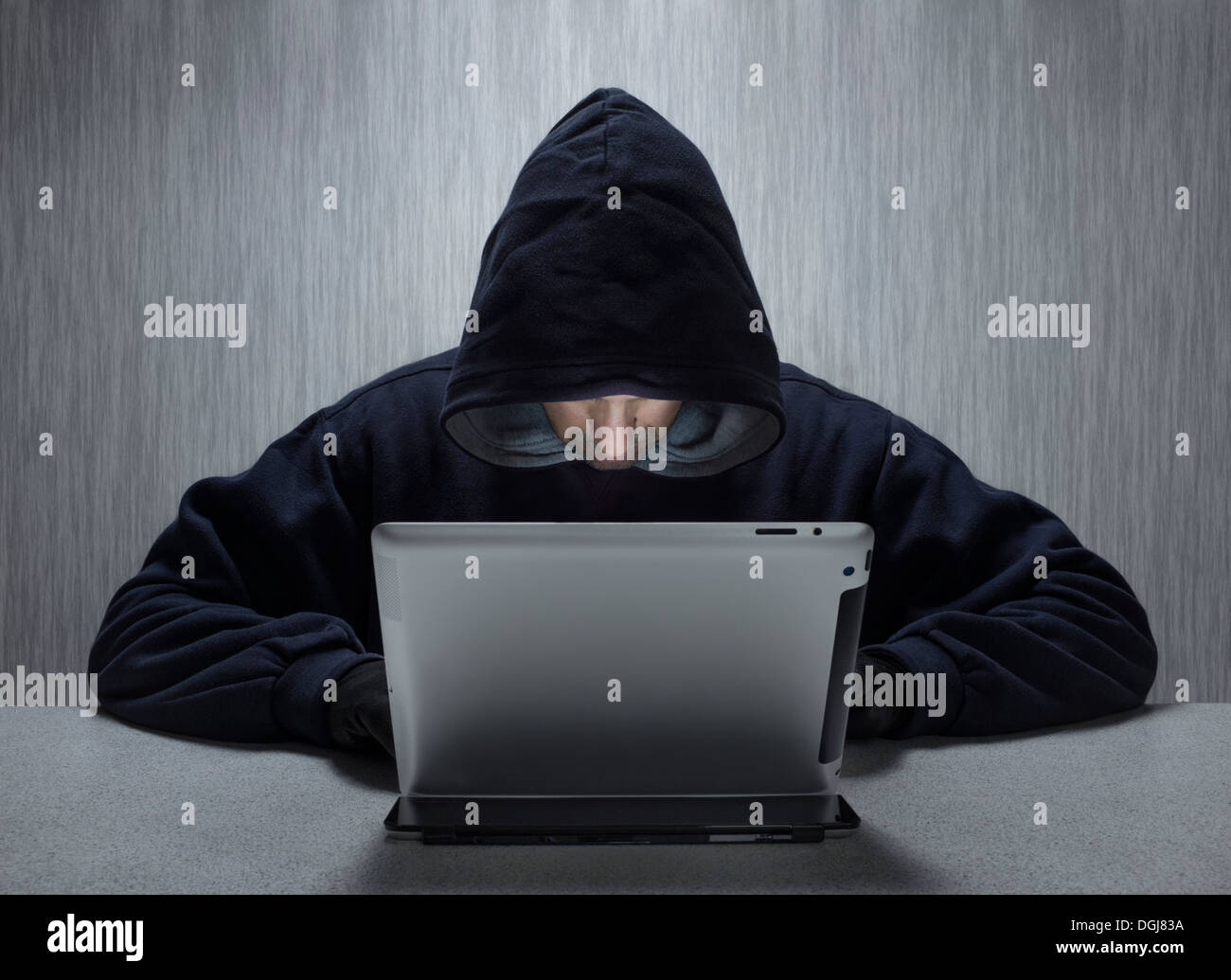 Un anónimo hombres encapuchados utilizando un equipo de tableta para representar una Cyber criminales. Foto de stock