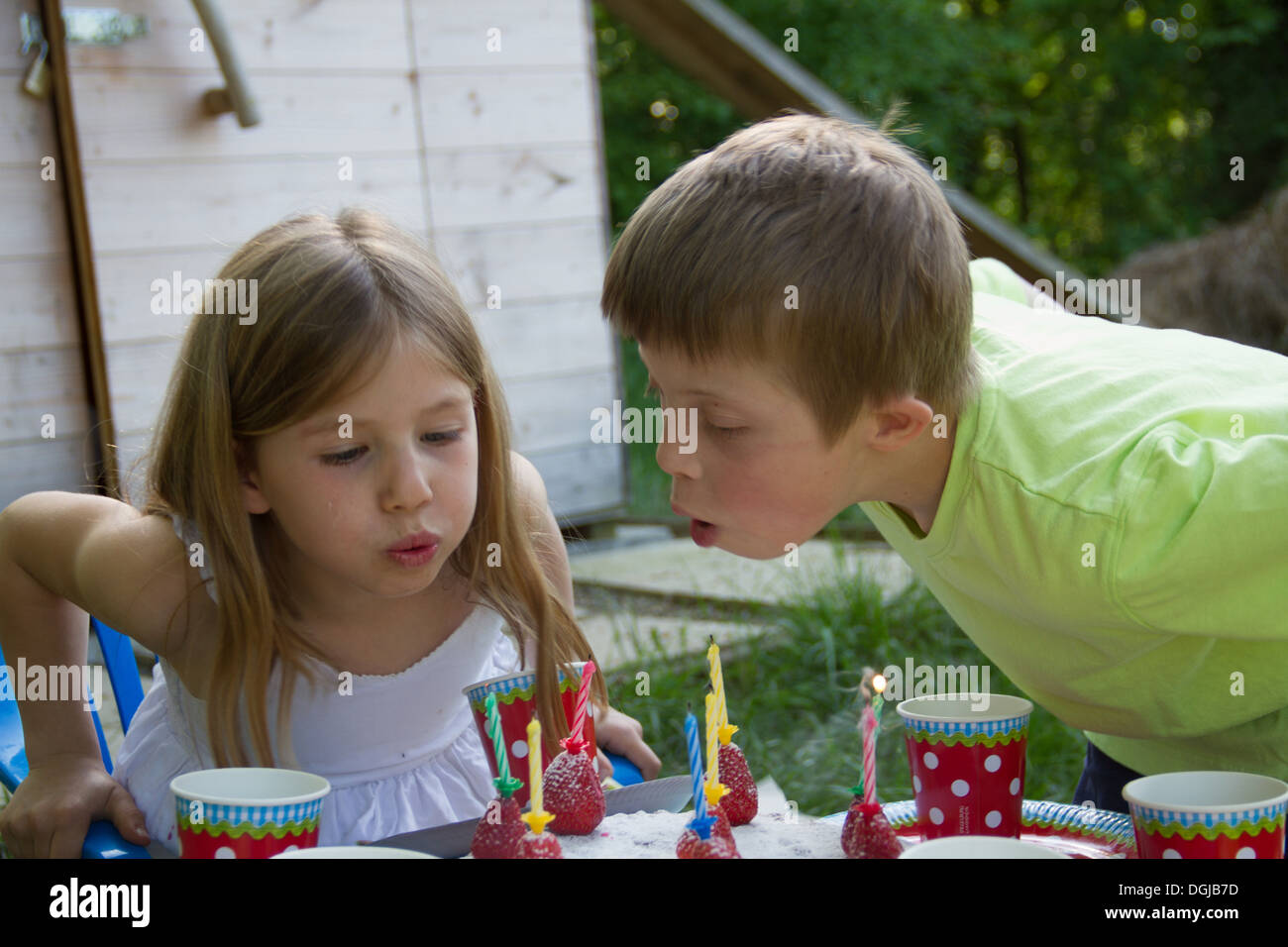 Garden Party familia compartiendo la torta de cumpleaños. El niño de 3 años  está disfrutando de su obra, el jardín está decorado con globos y los  colores son brillantes Fotografía de stock 