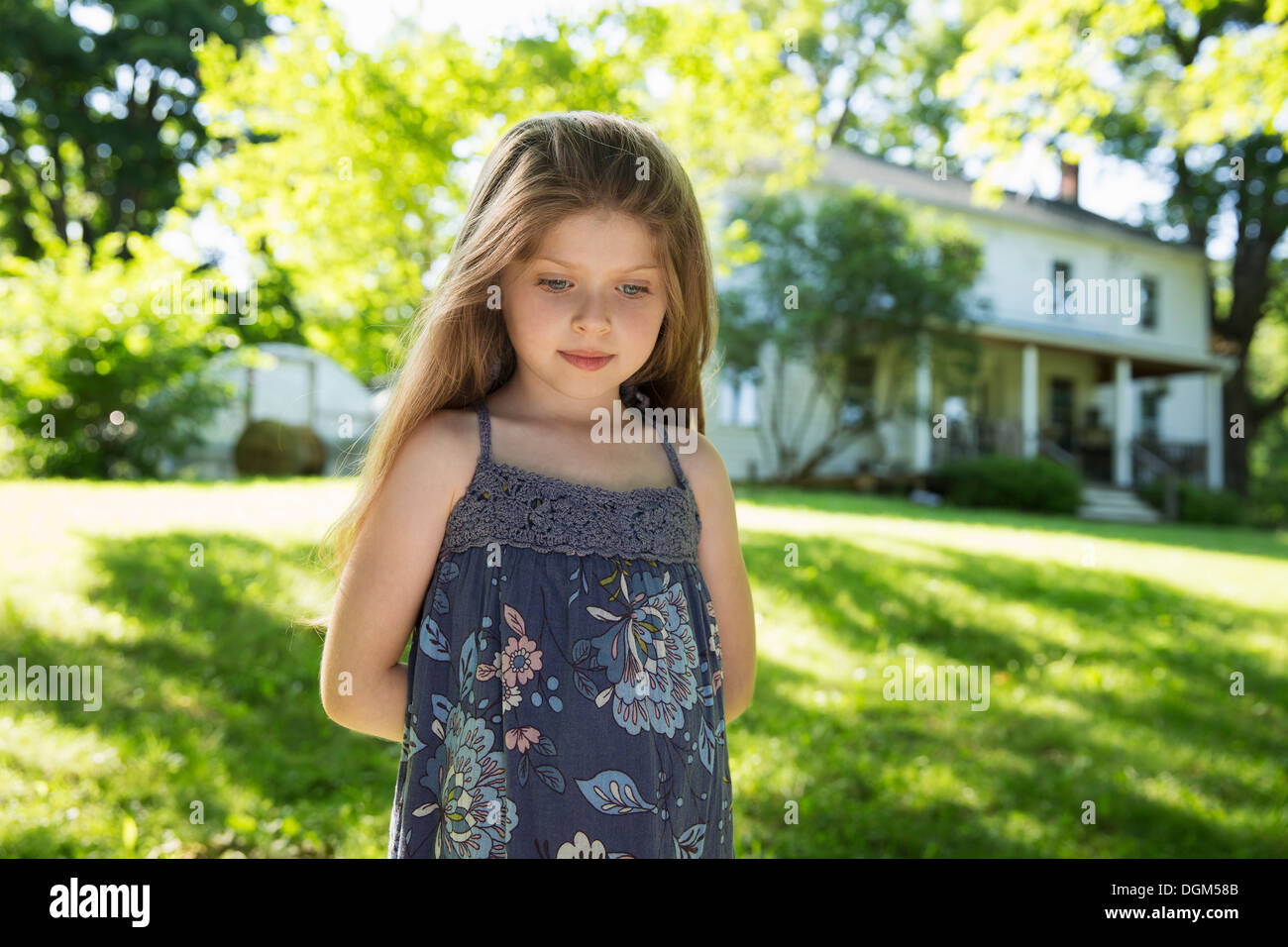Al aire libre en verano. En la granja. Una niña en el jardín con sus manos detrás de su espalda. Foto de stock