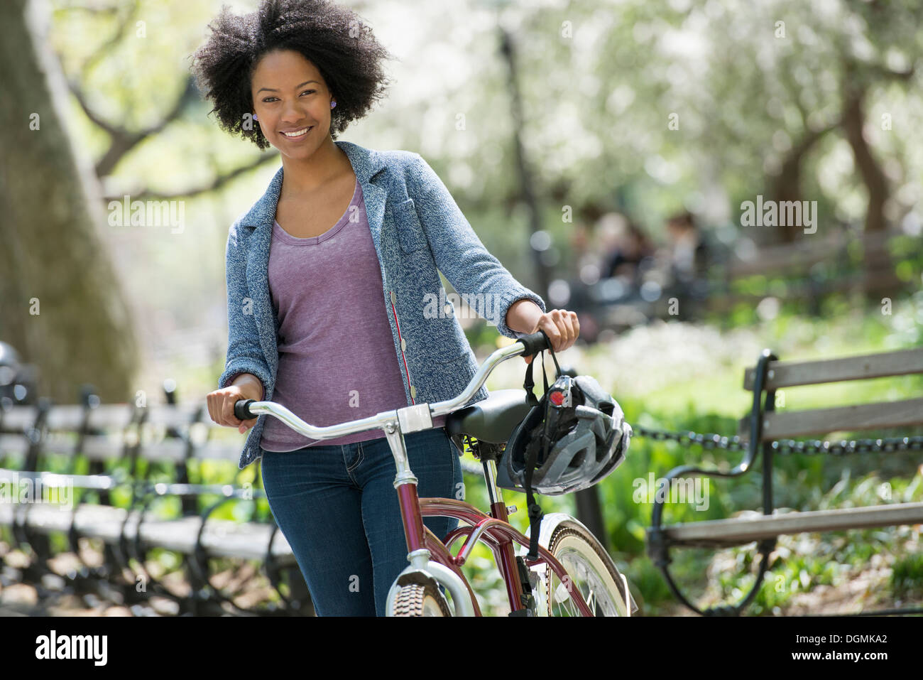 Una mujer en ropa casual en el parque empujando una bicicleta. Foto de stock