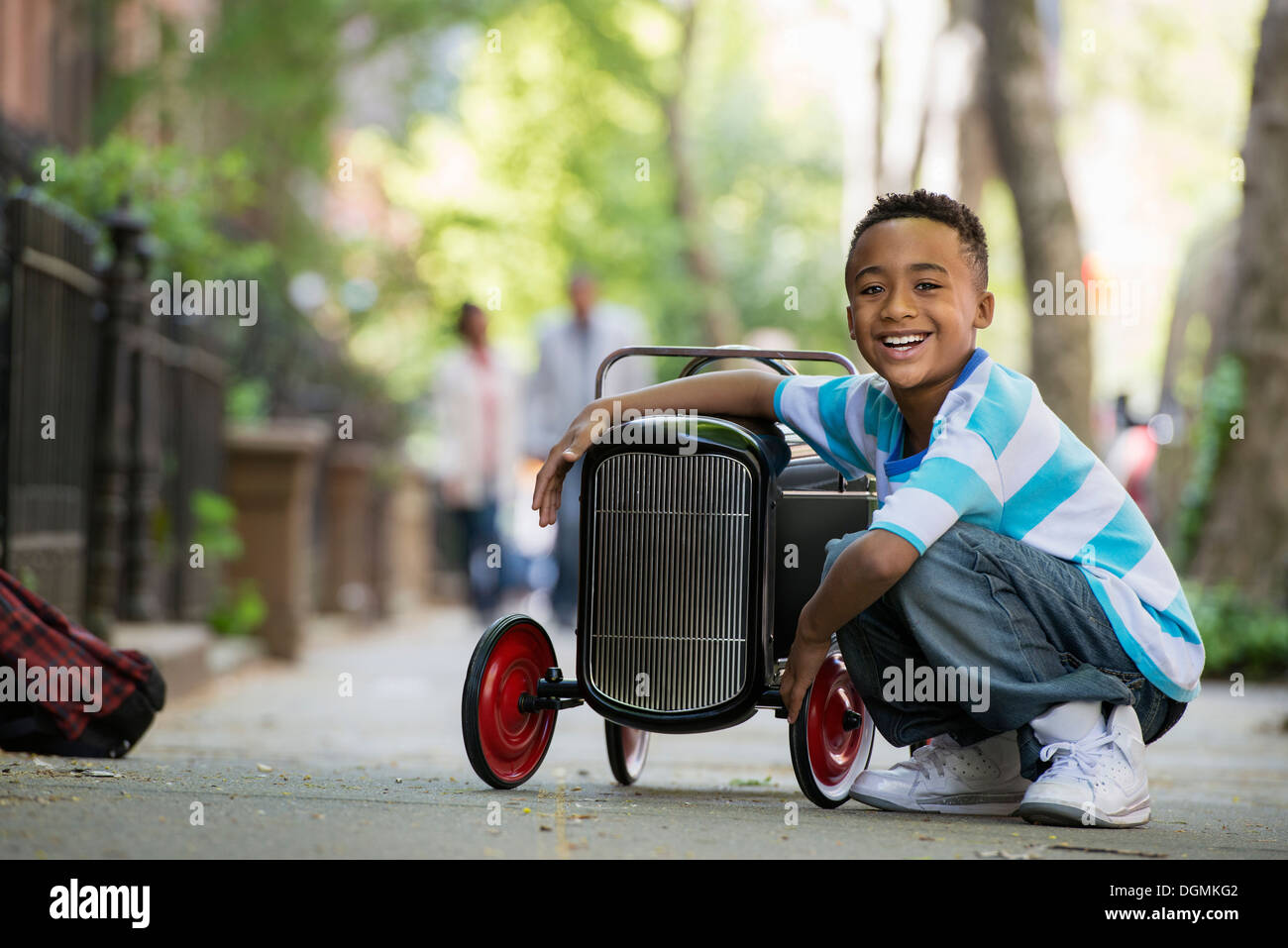 Un joven jugando con un viejo coche de juguete sobre ruedas en una calle de la ciudad. Foto de stock