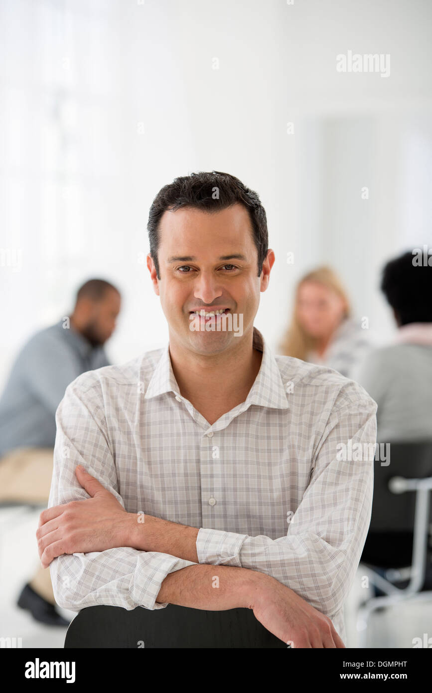 Oficina interior. Un hombre sentado por separado de un grupo de personas sentadas alrededor de una mesa. Una reunión de negocios. Foto de stock