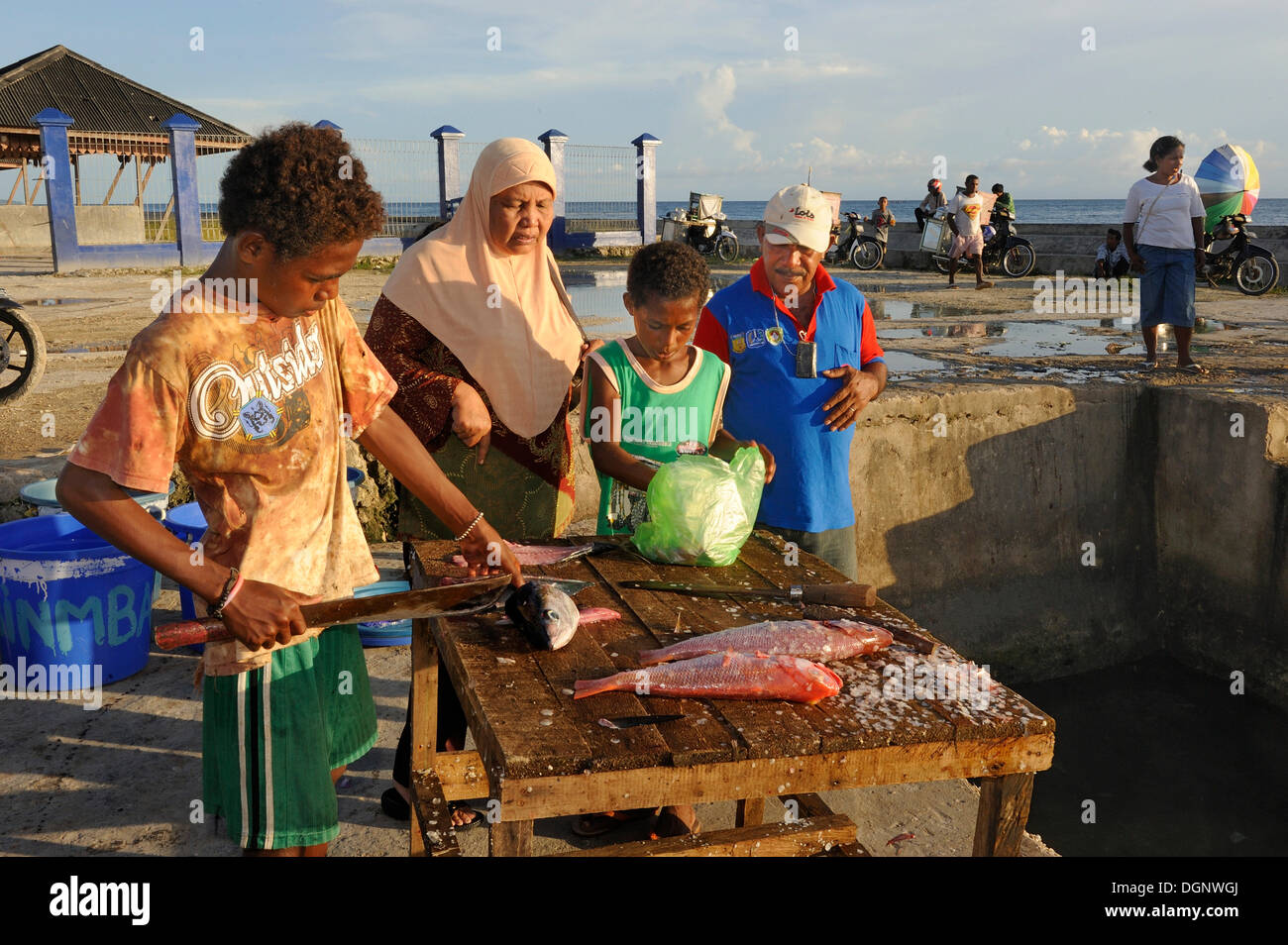 Los niños destripar pescado con un machete para un cliente musulmana cubierta con un velo, mercado de pescado en Kota Biak, Isla Biak Foto de stock