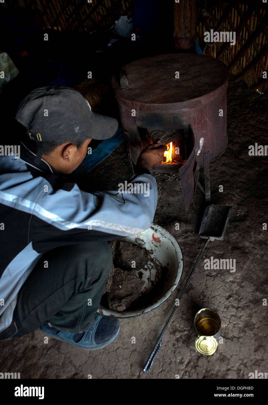 Chico con tapa poner estiércol en la estufa de la yurta, Saralasaz Jailoo, Kirguistán Foto de stock
