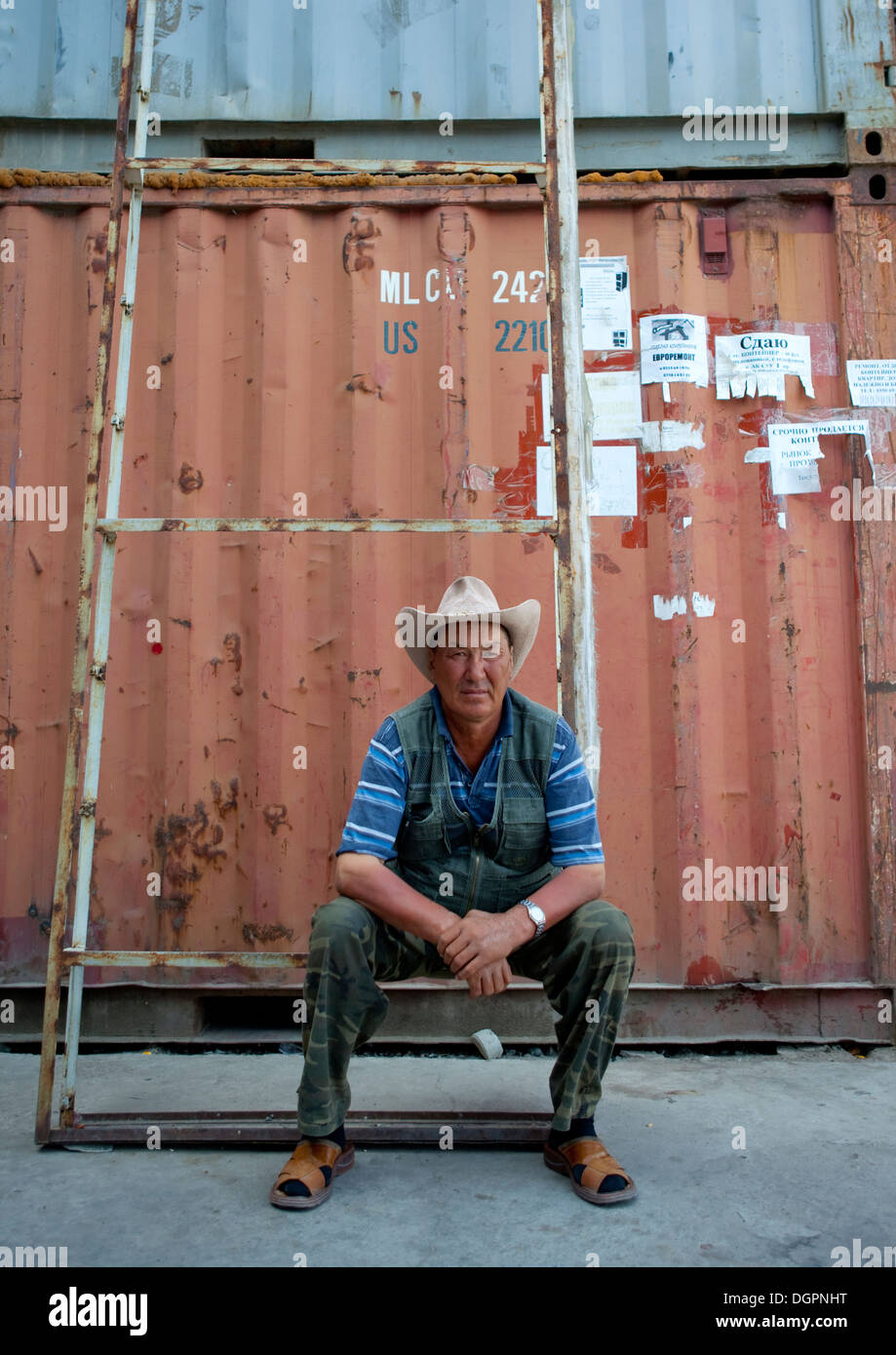 Hombre con un sombrero de Cow Boy sentado delante de un contenedor en el mercado Dordoi, Bishkek, Kirguistán Foto de stock