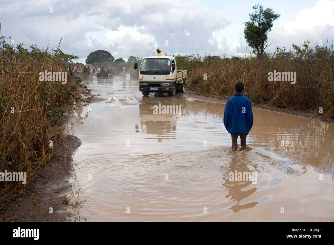 Mozambique, un hombre en una chaqueta azul de pie en un camino inundado en el monte, una camioneta tratando de cruzar. Foto de stock