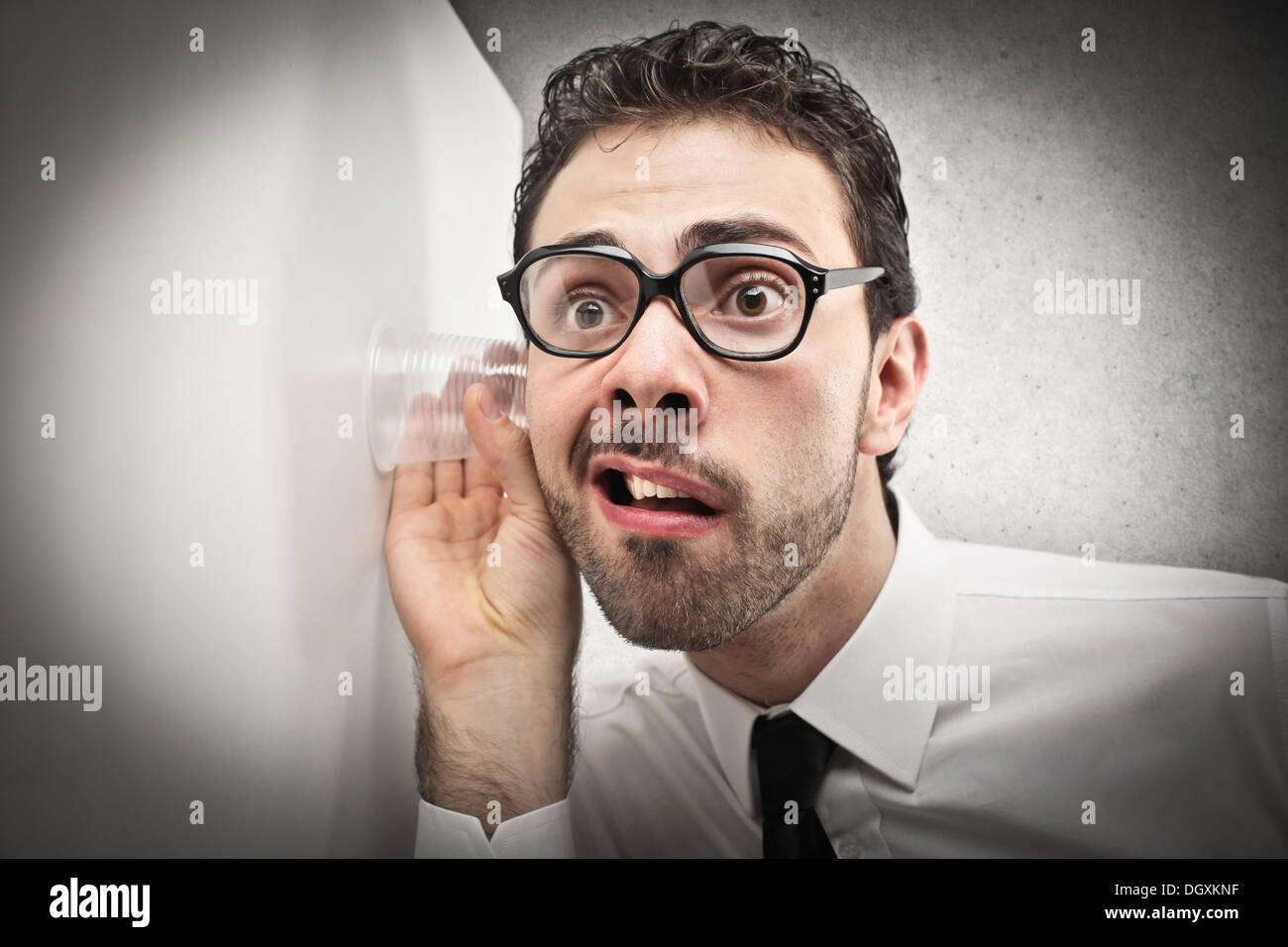 Trabajador de oficina con gafas, tratando de escuchar a través de una pared Foto de stock