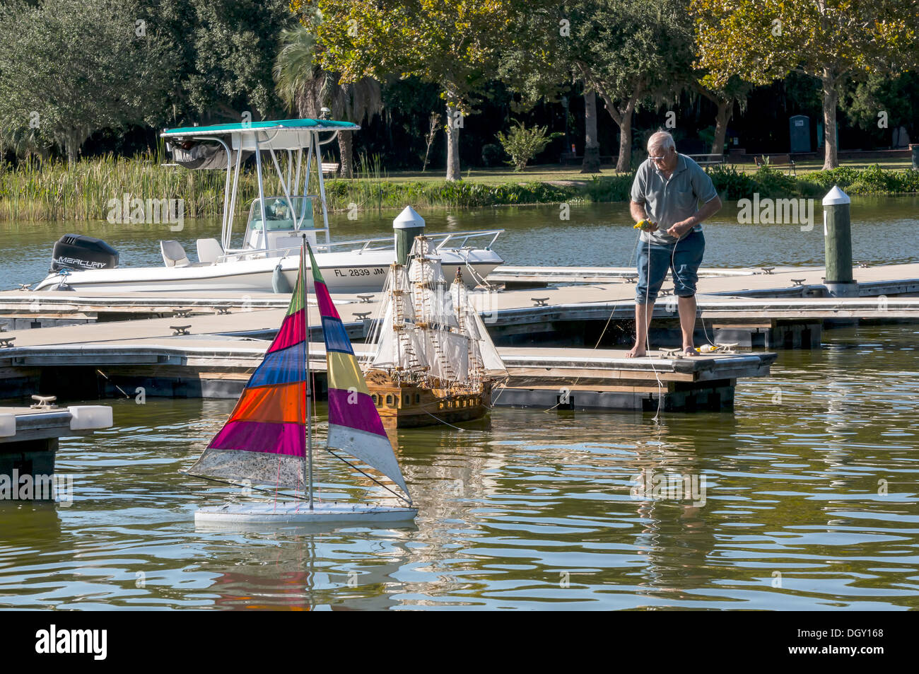 Hombre en el muelle lanza maquetas de sloop con rayas multicolores y velas galeón español barco velero en el lago Dora. Foto de stock