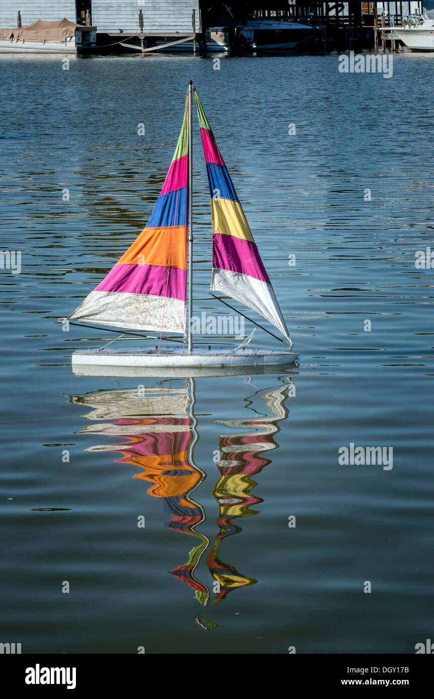 Modelo a escala de un barco de vela sloop con rayas multicolores velas flotantes en el lago Dora en el puerto de Mount Dora, Florida. Foto de stock