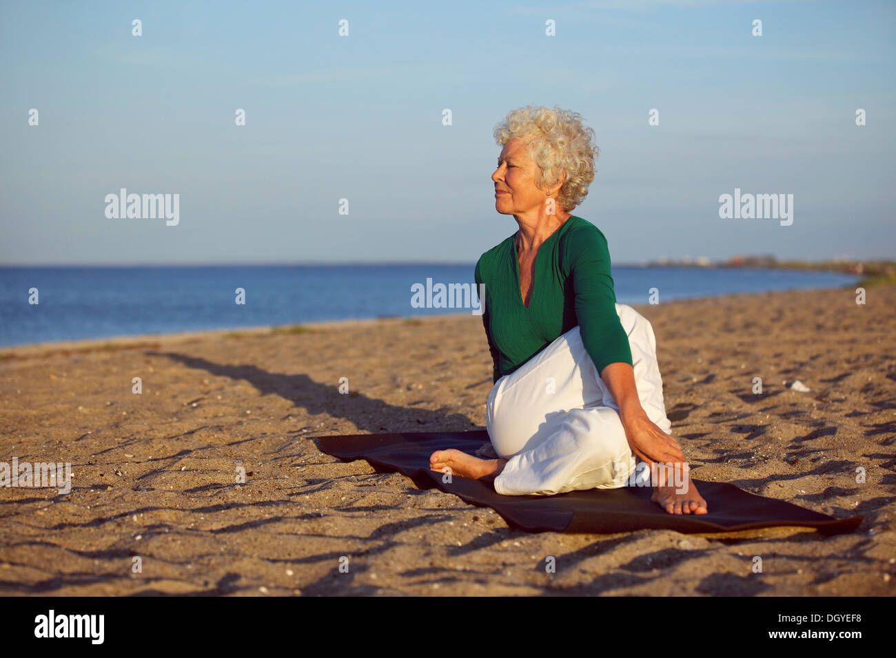 Mujer mayor realizando una rutina de yoga en la playa. Elder mujer haciendo ejercicio de estiramiento en la playa de arena con un montón de copyspace Foto de stock