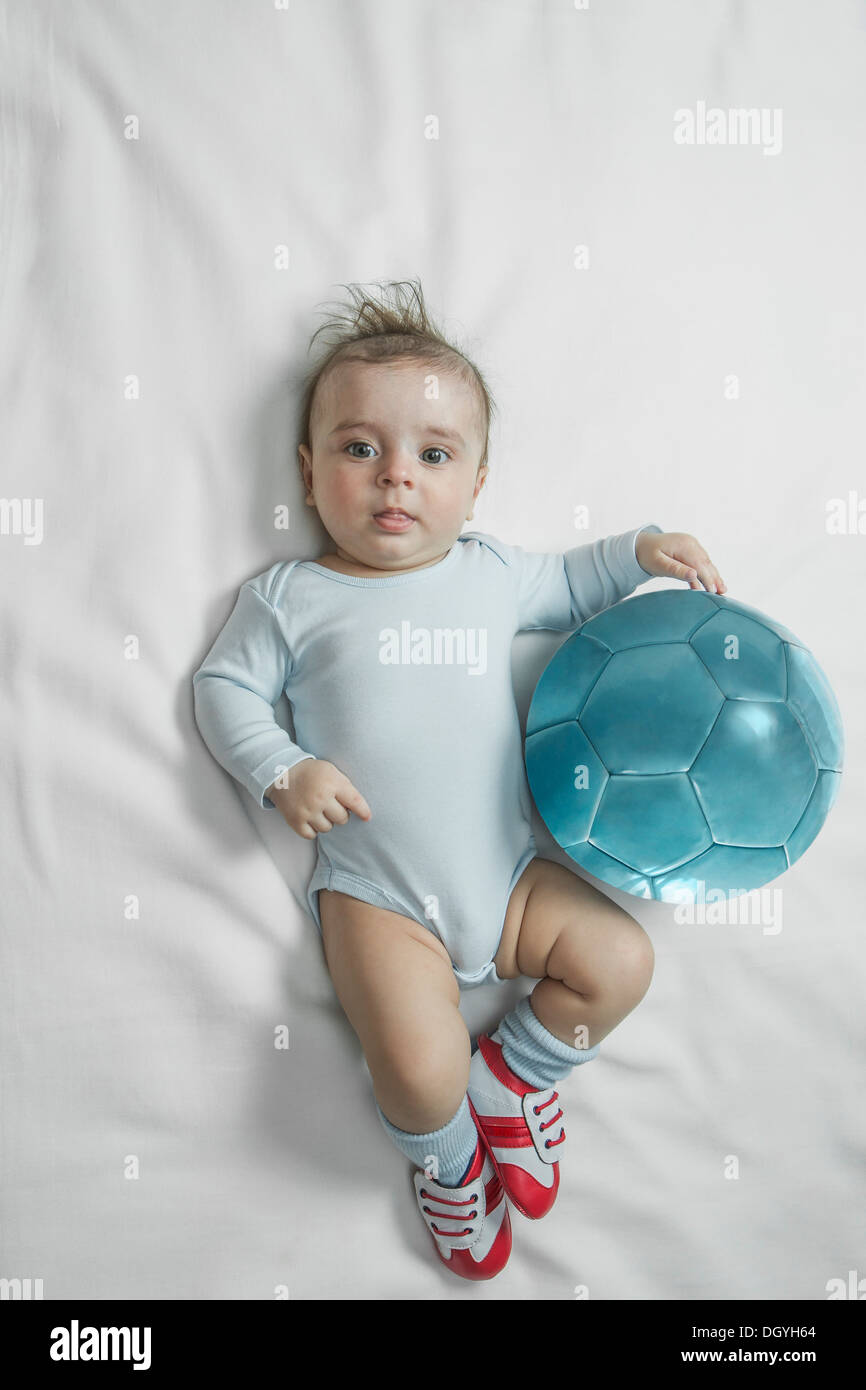 Un bebé bebé niño usando zapatos de fútbol tumbado junto a un balón de  fútbol Fotografía de stock - Alamy