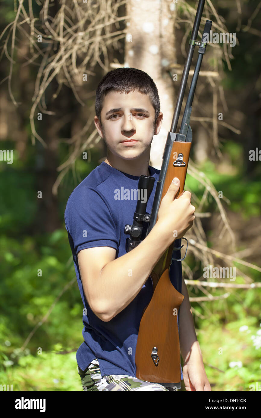 Niño con rifle óptico en el bosque Foto de stock