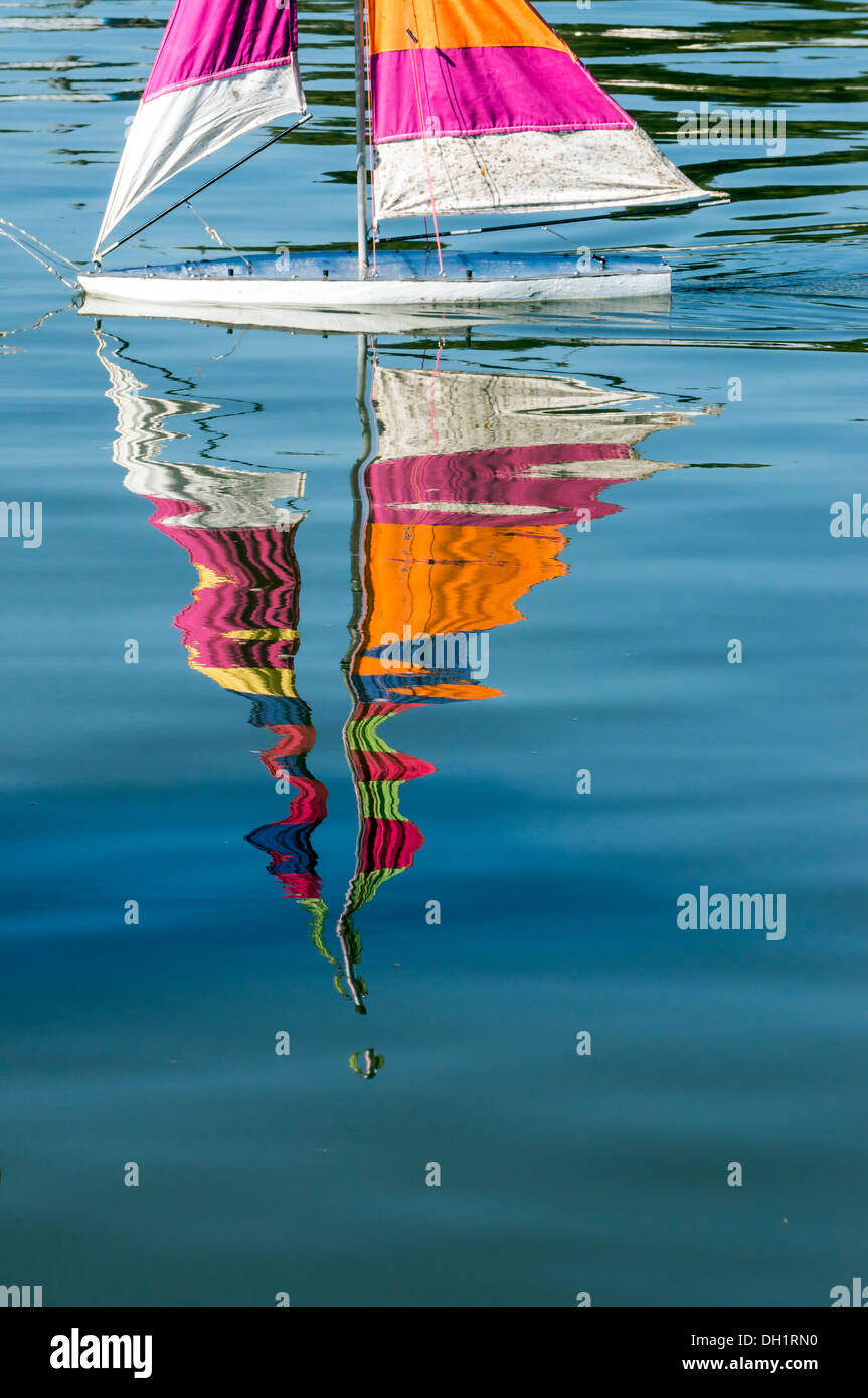 Reflexiones de un modelo a escala de juguete sloop velero con rayas coloridas velas en aguas color turquesa. Foto de stock