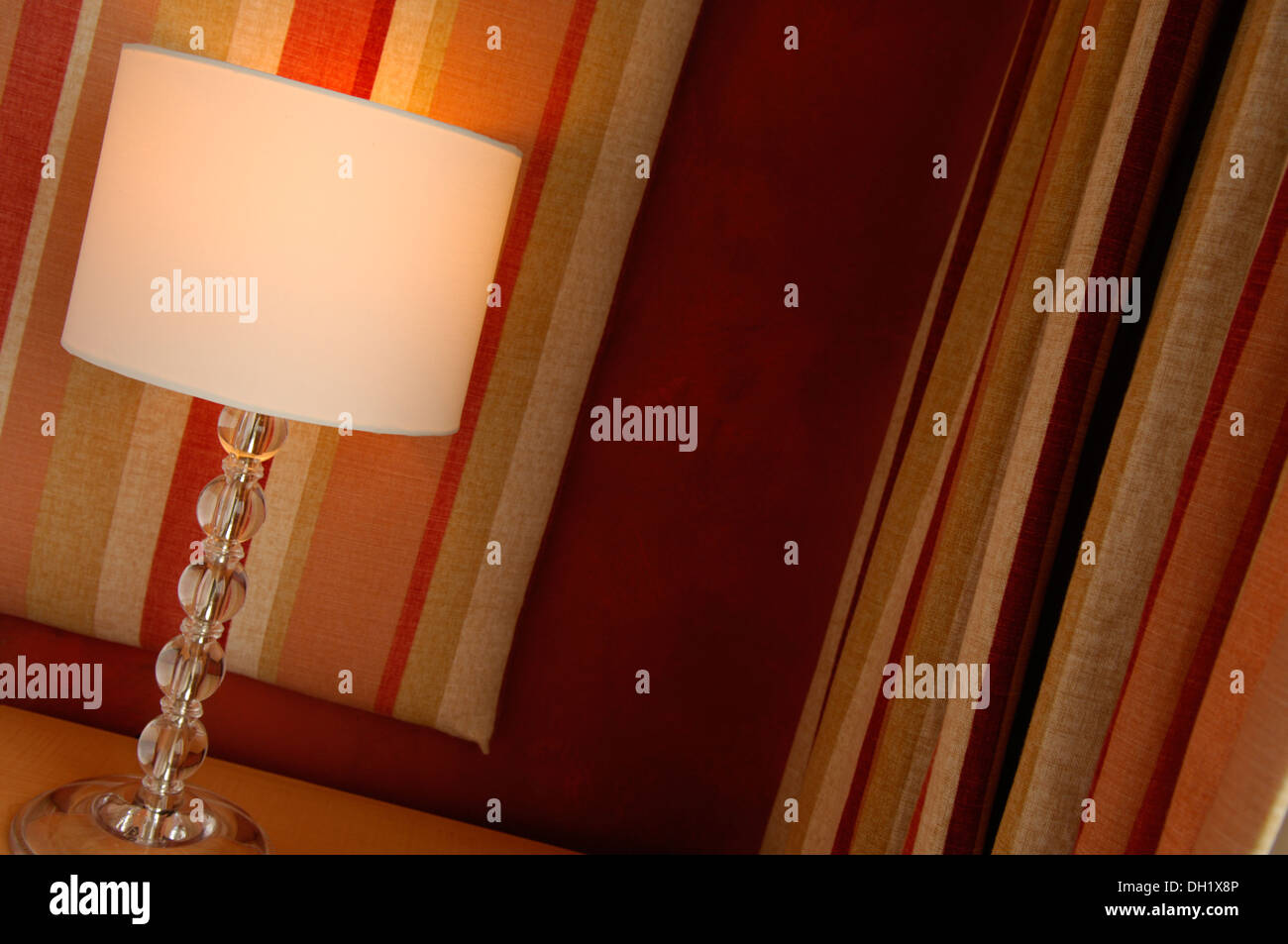 Una lámpara de mesa con un vaso de cebada twist, cortinas rayadas verticalmente. Foto de stock