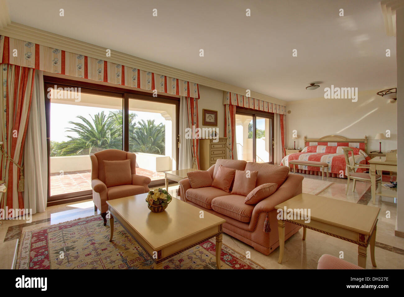 Cortinas de rayas en puertas de cristal al balcón en español apartamento  dormitorio con sofá y sillón rosa junto a café tabla de madera Fotografía  de stock - Alamy