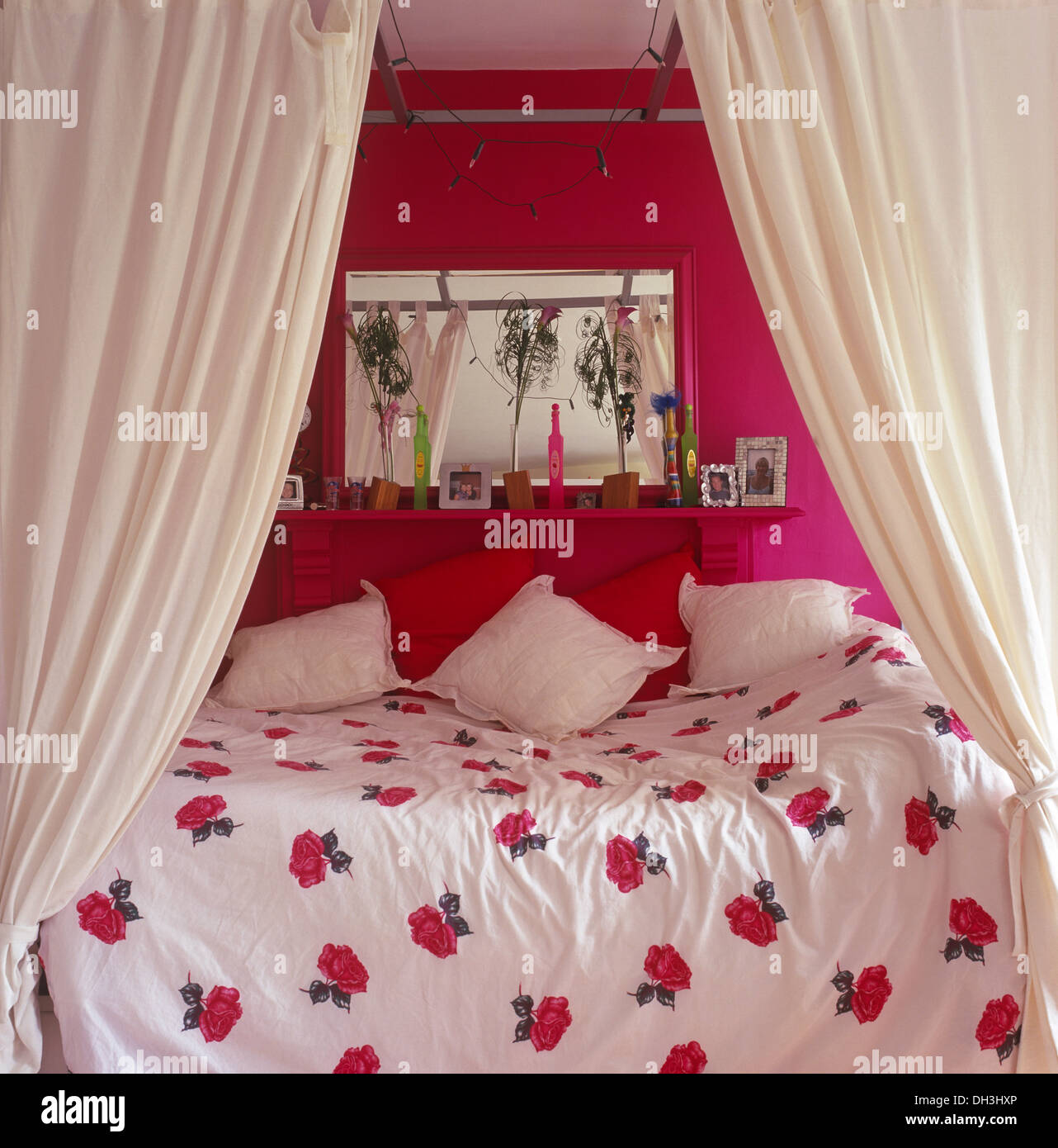 Cortinas blancas en una simple cama con dosel con cojines blancos y  rosa-telas edredón debajo de espejo sobre el estante en rosa dormitorio  Fotografía de stock - Alamy