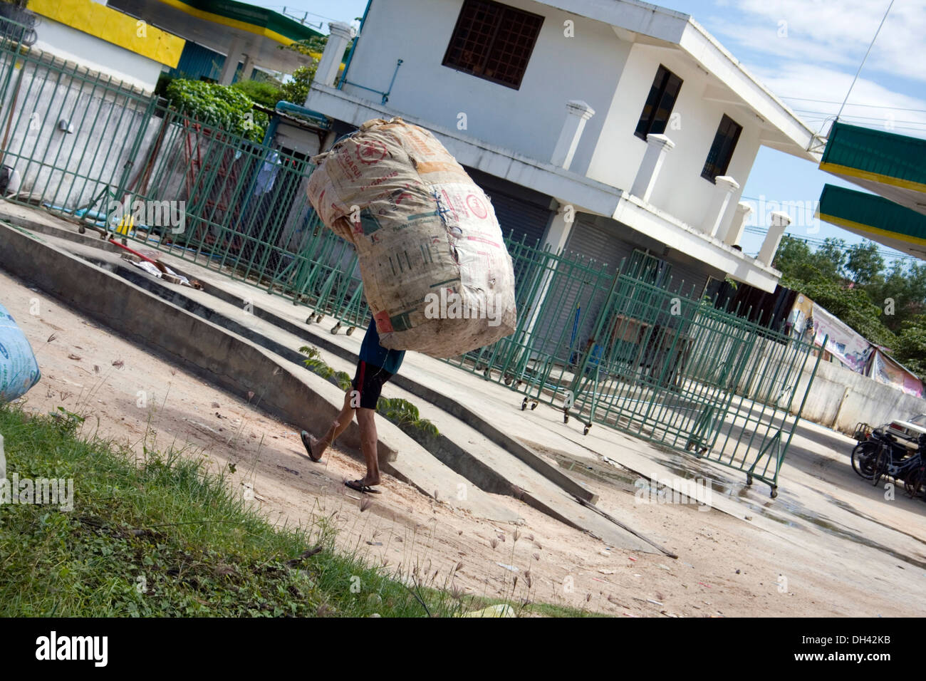 Es un hombre que llevaba una pesada bolsa llena con material reciclable cerca de un almacén de reciclaje de basura en Phnom Penh, Camboya. Foto de stock