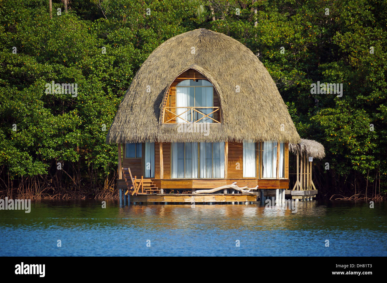 Bungalows con techo de paja sobre el agua con una exuberante vegetación tropical en el fondo, Bocas del Toro, Caribe, América Central, Panamá Foto de stock