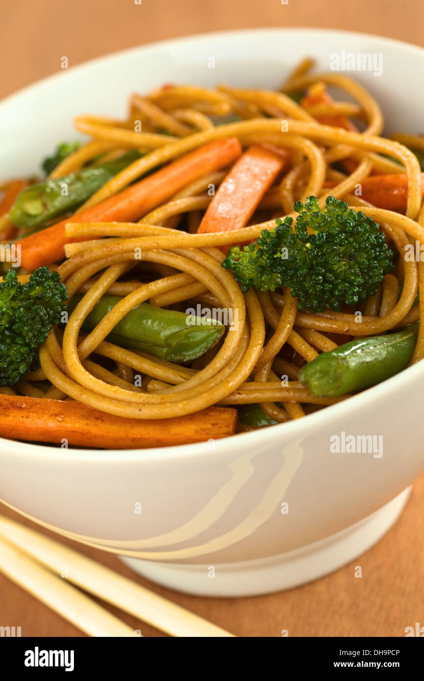 Espagueti integral y vegetales salteados en tazón blanco con palillos Foto de stock