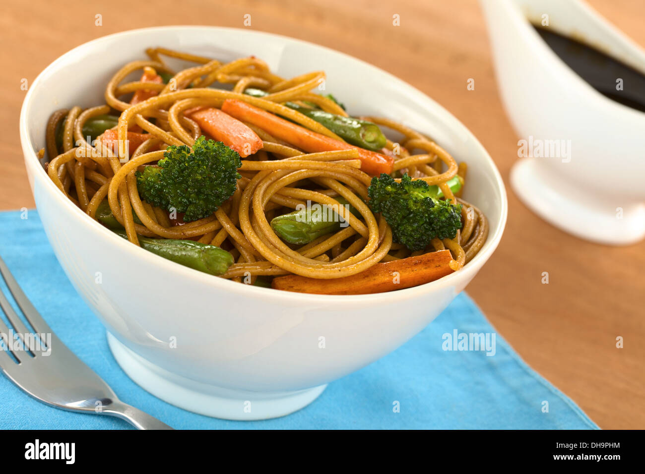 Espagueti integral y vegetales salteados en tazón blanco con salsa de soja en la espalda Foto de stock