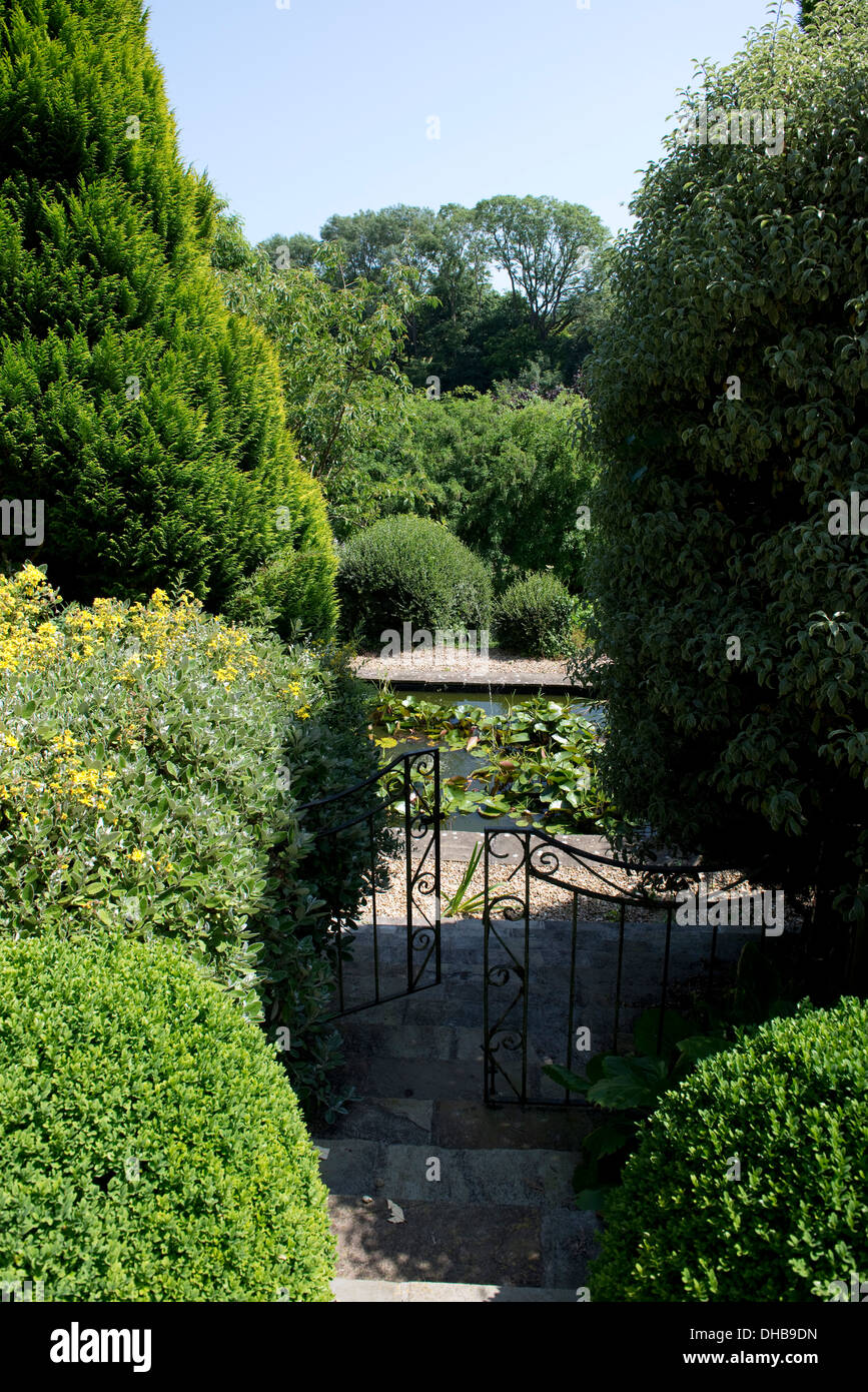 Pasos del jardín a través de los arbustos que conducen a través de una puerta a un estanque Foto de stock