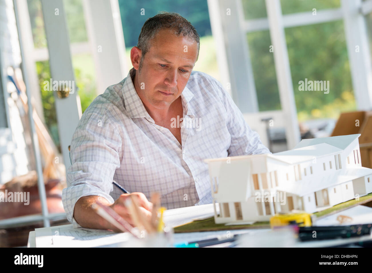 Una granja de cocina. Un modelo de una casa sobre la mesa. Diseñar una casa. Un hombre usando un dibujo a lápiz sobre un plan. Foto de stock