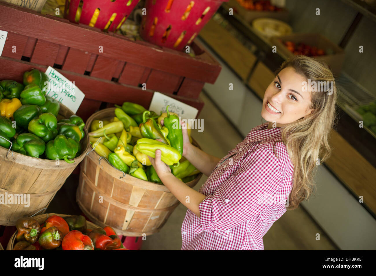 Trabajando en una granja orgánica. Una joven mujer de pelo rubio clasificar distintos tipos de pimiento por la venta. Foto de stock