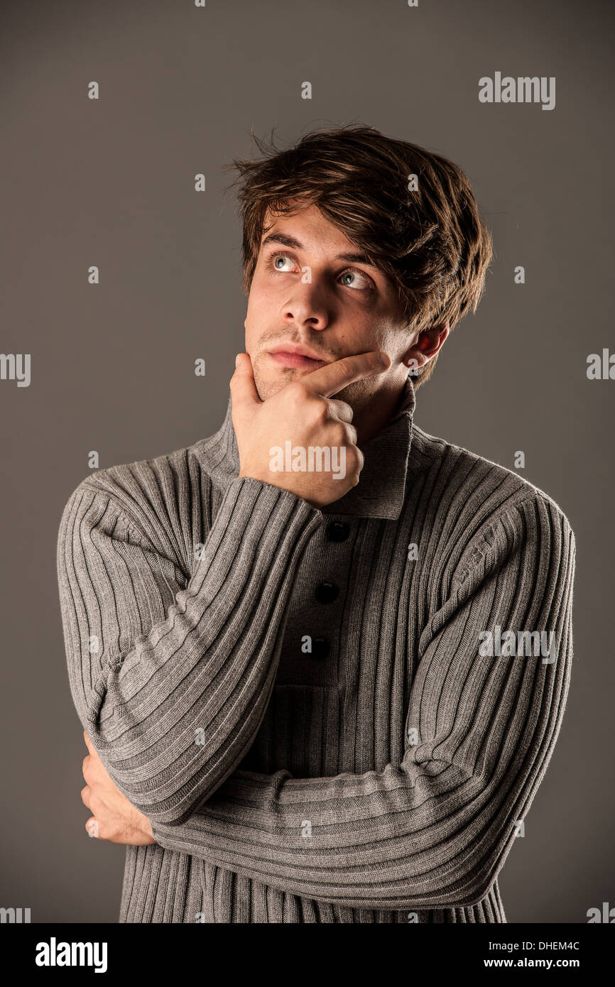 Pensativo joven suéter gris sobre fondo gris Foto de stock