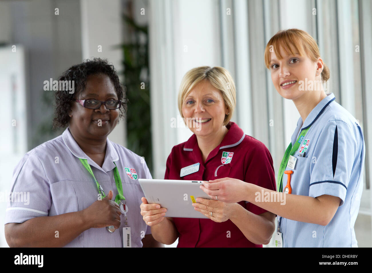 Un grupo de tres enfermeras discutir trabajos en un ordenador tablet UK Foto de stock