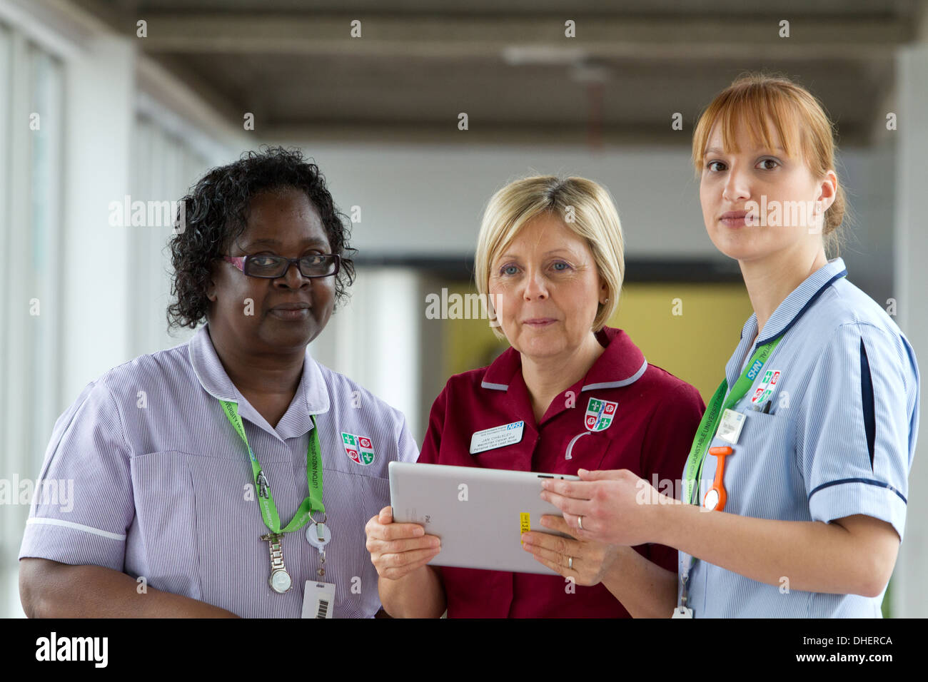 Un grupo de tres enfermeras discutir trabajos en un ordenador tablet UK Foto de stock