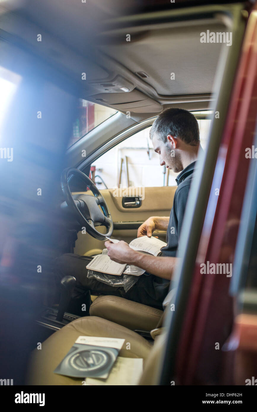 Mechanic sentado en el asiento del conductor de coche con manual. Foto de stock