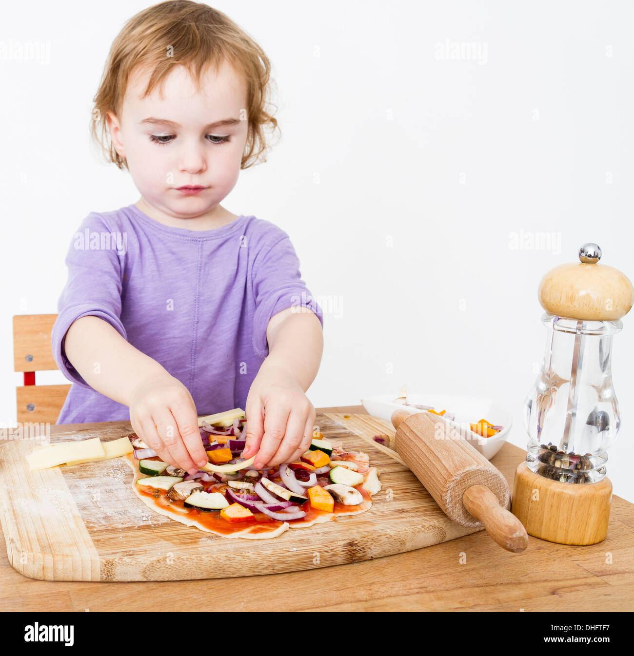 Cute Little Girl preparando pizza fresca en fondo gris neutro Foto de stock