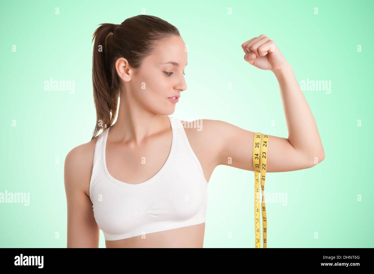 Mujer poderosa midiendo sus bíceps con una cinta de medición amarilla en un fondo verde Foto de stock