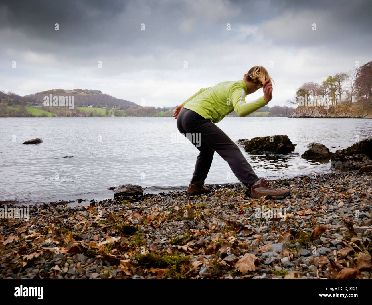 Niña de doce años arrojando piedras para hojear sobre el agua en el lago Ullswater en el Lake District National Park Cumbria Inglaterra Foto de stock
